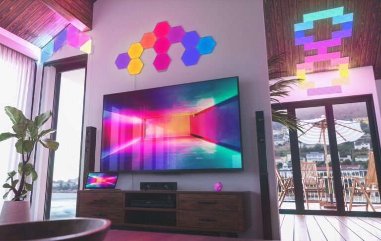 Salotto moderno con pannelli luminosi Nanoleaf Shapes a parete e a soffitto sopra una TV.