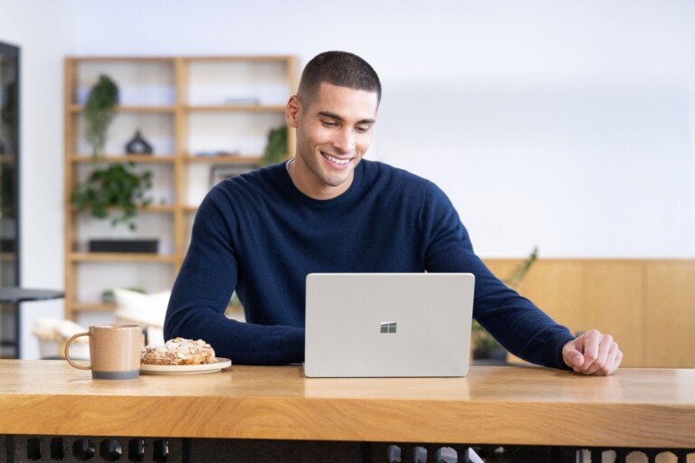 Un uomo sorride davanti a un computer portatile con il logo Microsoft in un ufficio moderno.