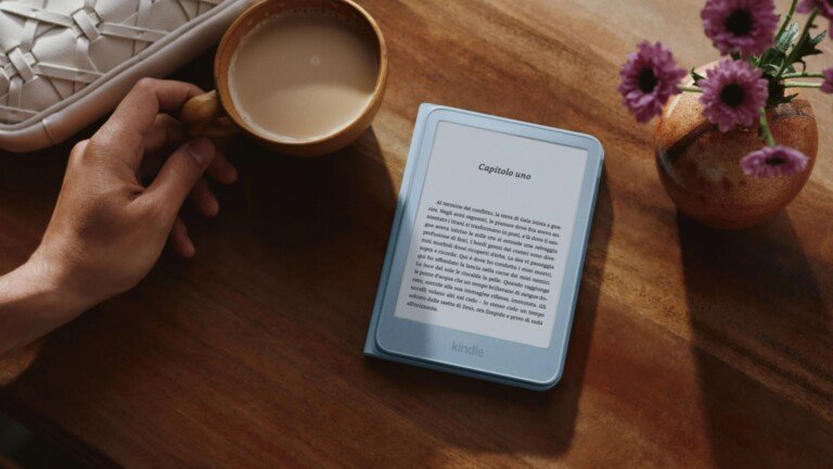 Un nuovo Kindle azzurro su un tavolo in legno accanto a una tazza di caffè e dei fiori.