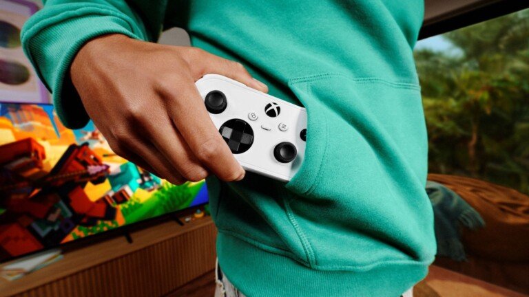 Una mano infila il piccolo controller bianco Xbox Nano nella tasca di una felpa verde.