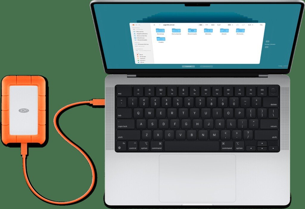MacBook aperto e collegato tramite cavo arancione a un hard disk esterno portatile.