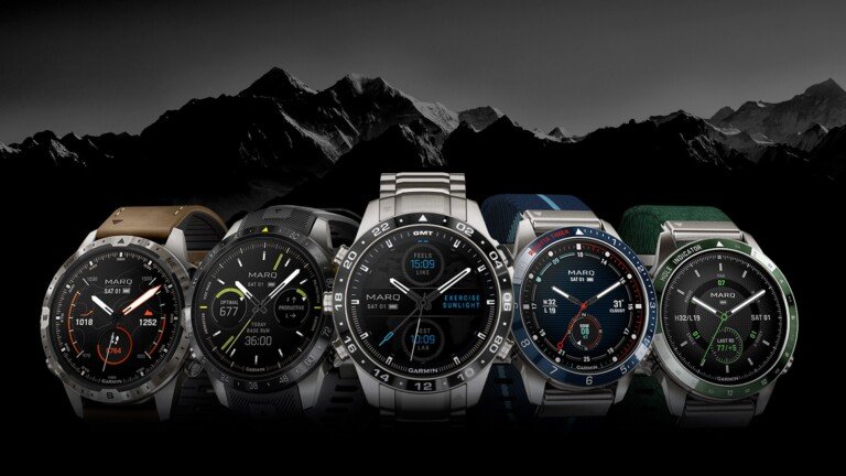 Panoramica della collezione di smartwatch Garmin MARQ disposti in fila su sfondo montano.